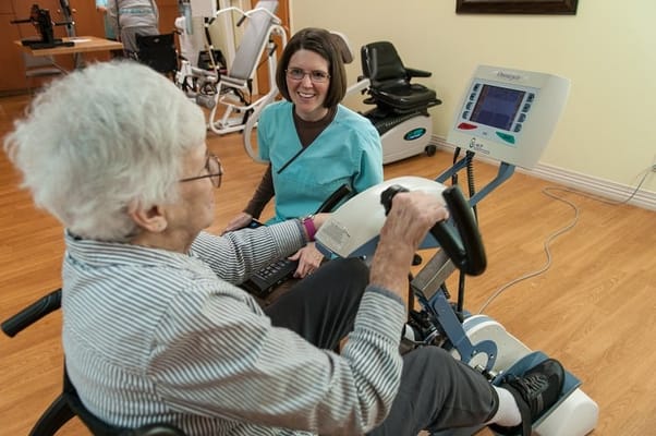 Staff assisting resident with therapeutic exercise equipment