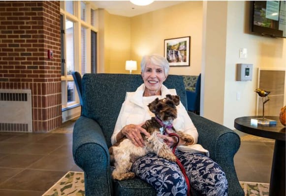 A resident smiling with a dog in a cozy lounge area