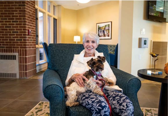 A resident smiling with a dog in a cozy lounge area