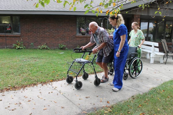 Staff assisting a resident outdoors with a walker