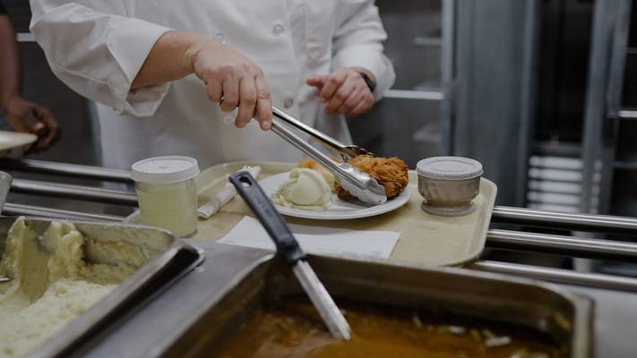 Staff serving food on a tray in a kitchen setting
