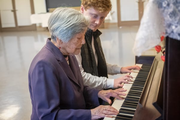 An older woman playing piano with a younger man