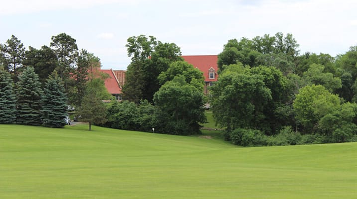 View of facility building behind green lawns and trees