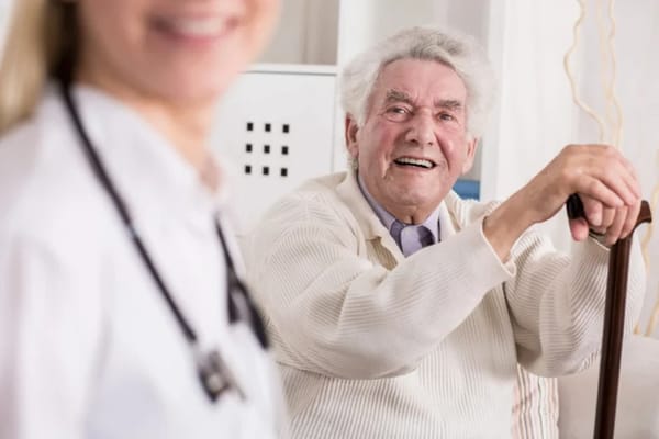 A senior man smiling while sitting with a caregiver