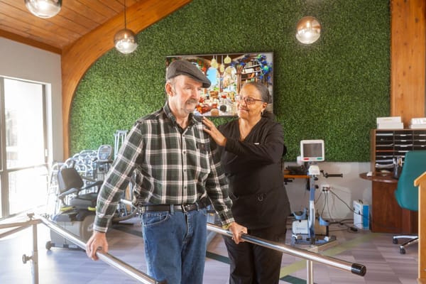 Therapist assisting an elderly man with walking.
