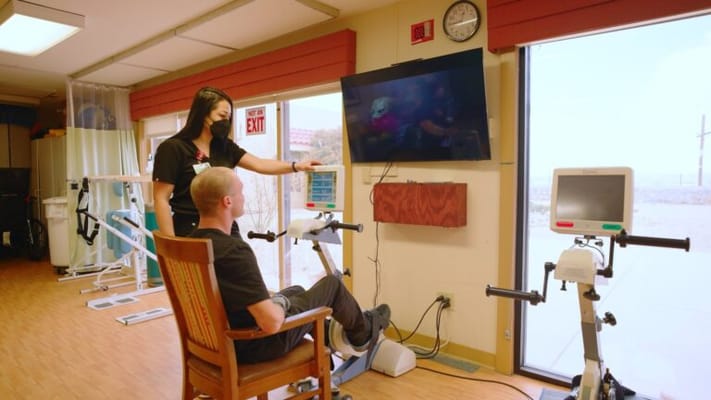 Staff assisting a resident with therapy equipment in a well-lit room