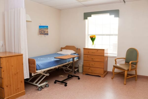 A private resident room with a bed, dresser, and flower vase