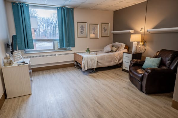 A well-furnished resident room with a bed and chair