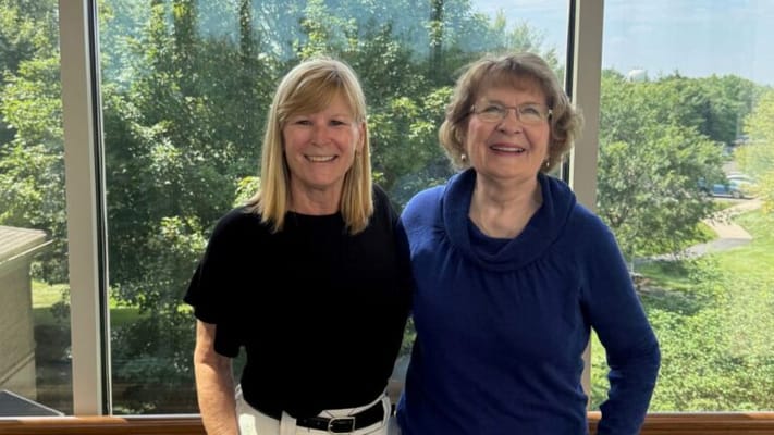 Two residents smiling together by a large window