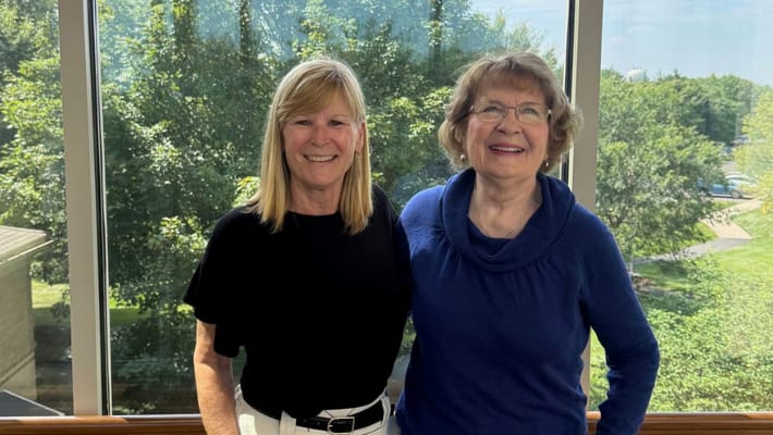 Two residents smiling together by a large window
