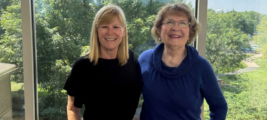 Two women smiling together in a sunny interior space