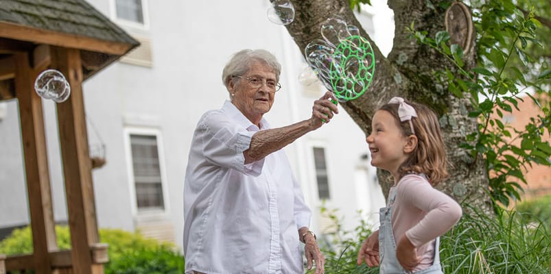 An elderly woman bubbles with a young girl outdoors