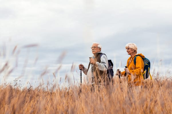 Two seniors hiking through a grassy field