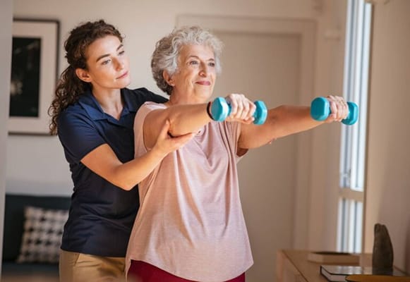 A caregiver assisting a senior woman with light weights