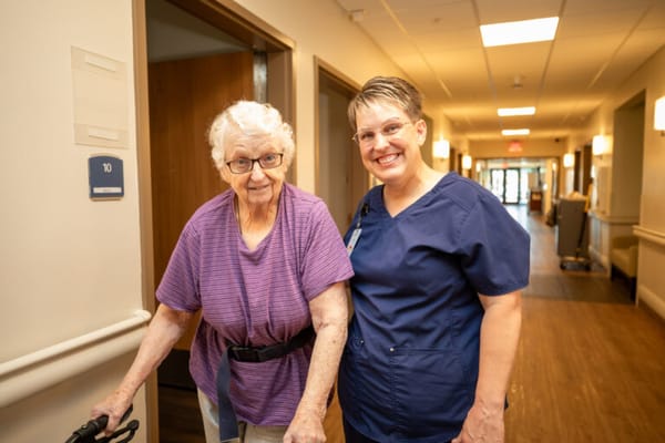 Resident and staff member smiling in a hallway