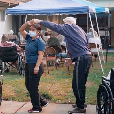 An elderly man gracefully dancing with a staff member outdoors