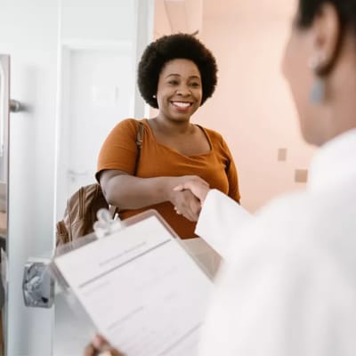 Smiling woman greeting staff with a handshake in a bright lobby