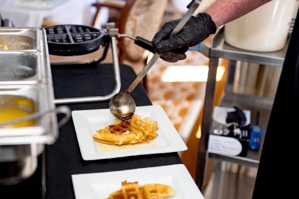 A staff member serving waffles with syrup in a dining area