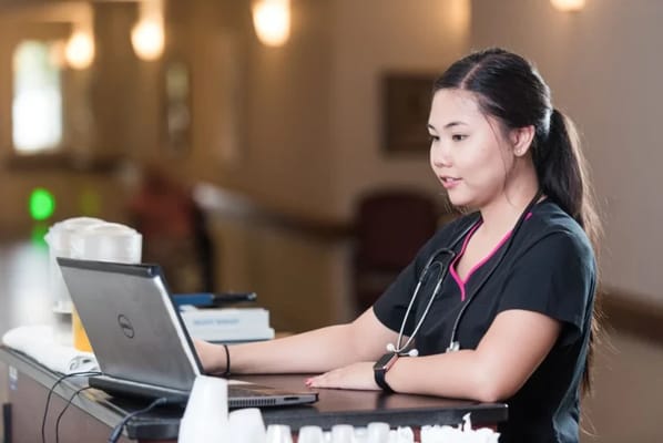 Nurse assisting at a reception area with a laptop