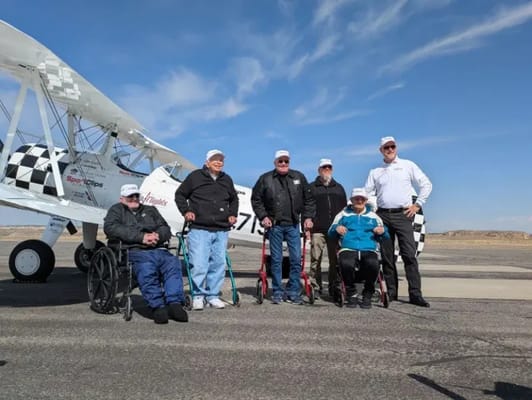 Residents enjoying a special outing with pilots next to a biplane