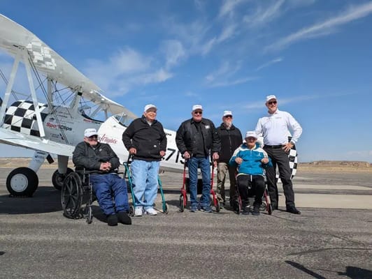 Residents enjoying a special outing with pilots next to a biplane