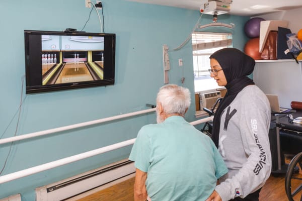 Resident participating in a bowling activity with staff assistance