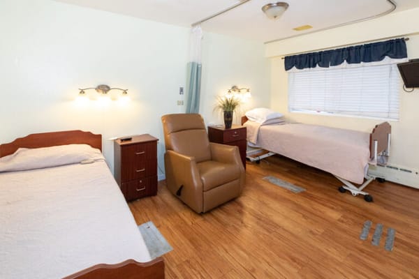 A shared resident room with two beds and a recliner