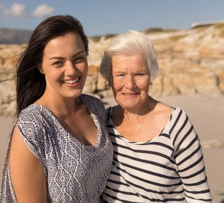 An older woman and a younger woman smiling together at the beach