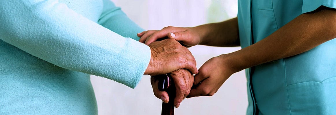 Hands of a caregiver assisting a senior with a cane