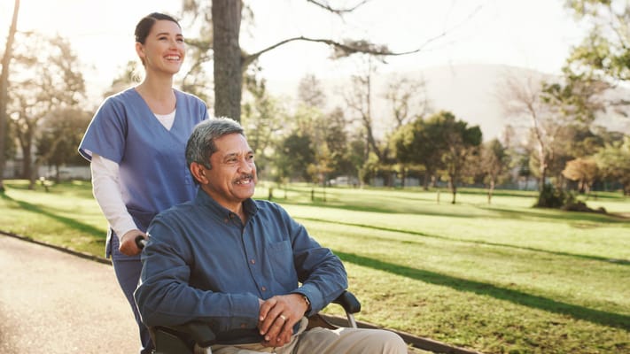 Caregiver pushing a resident in a wheelchair through a park