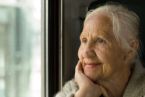 Elderly woman gazing out a window, lost in thought