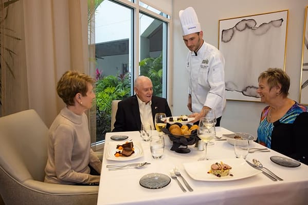 Residents enjoying a meal served by staff in a dining area