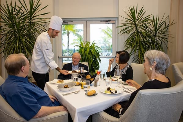 Residents enjoying a meal with a chef in a dining room