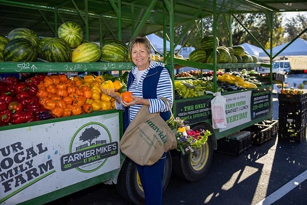 A woman at a farmer's market surrounded by fresh produce
