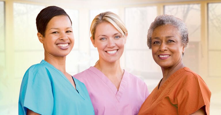 Three smiling nursing staff members in scrubs