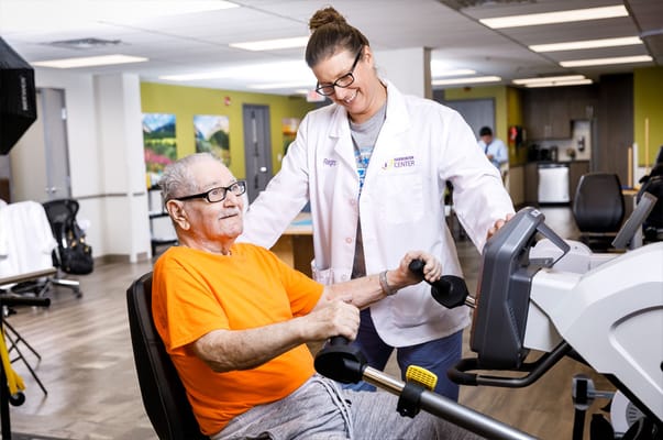 A resident using exercise equipment with a staff member's assistance