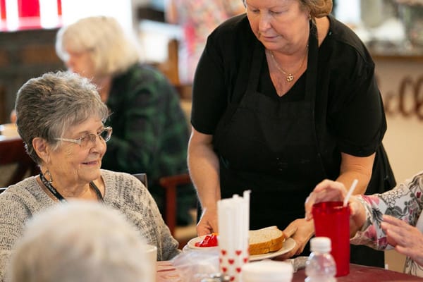 Staff serving a meal to a resident in a dining area