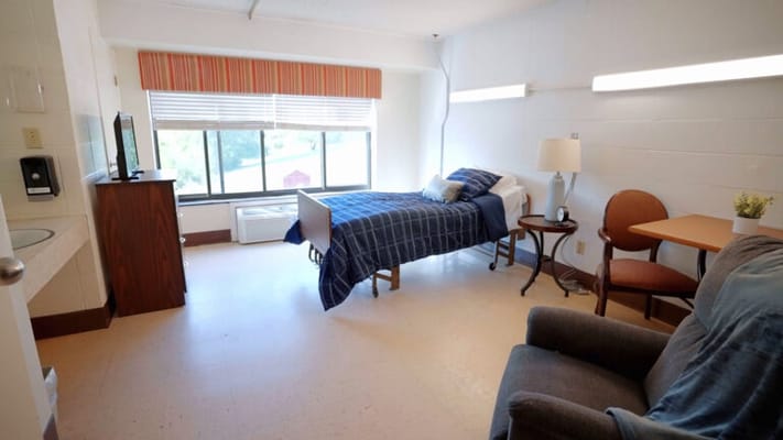 A private resident room featuring a bed and sitting area