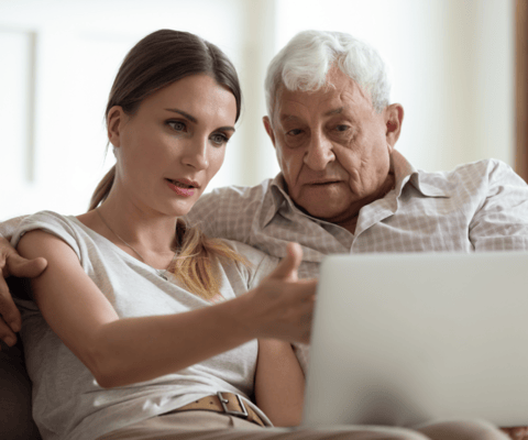 A caregiver assisting an elderly man with a laptop