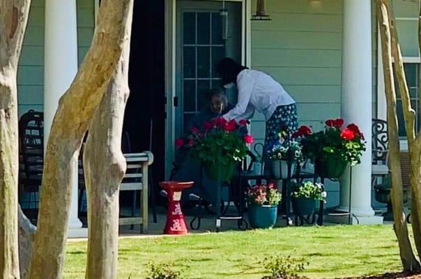 A staff member assisting a resident on a porch with flowers