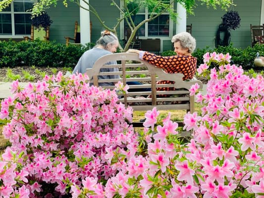 Two residents enjoying a garden bench surrounded by flowers