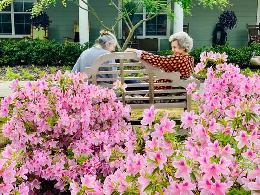Two residents enjoying a garden bench surrounded by flowers