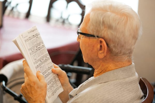 Elderly man holding sheet music in a common area