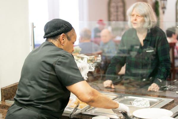 Staff serving food in a dining area with residents in the background