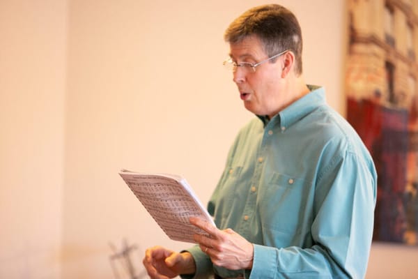 A man singing with sheet music in a facility interior