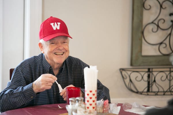 A smiling senior man in a red cap enjoying a meal