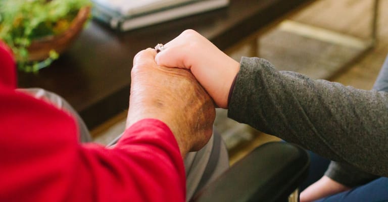 An elderly hand holding a younger hand, symbolizing care