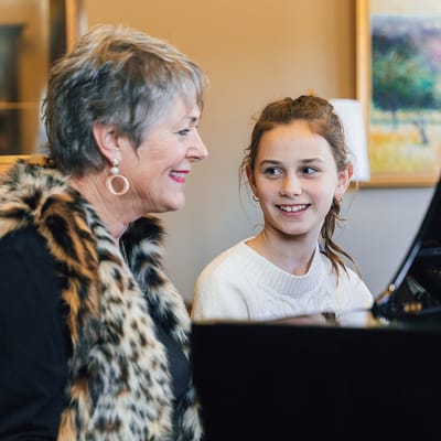 An older woman and a young girl playing piano together