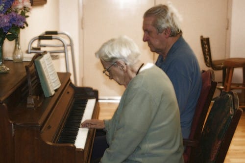 Residents enjoying music at a piano in a common area.