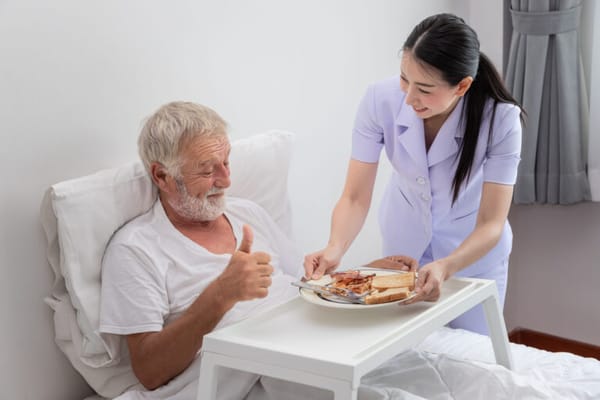Nurse serving food to a smiling resident in bed